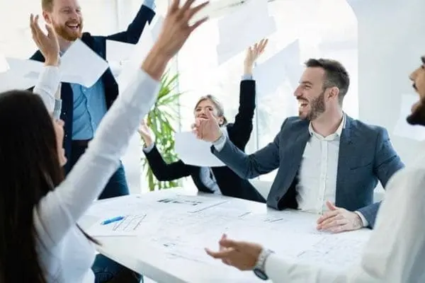 Imagem mostrando pessoas comemorando em um ambiente de escritório moderno, representando a realização de abrir uma empresa no Brasil. A cena reflete o entusiasmo e o senso de conquista associados ao início de um novo negócio, destacando a união e o trabalho em equipe necessários para superar desafios burocráticos e alcançar o sucesso empresarial
